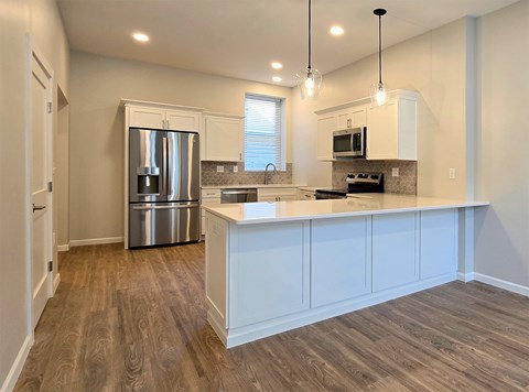 A kitchen with a stainless steel refrigerator and wooden flooring.